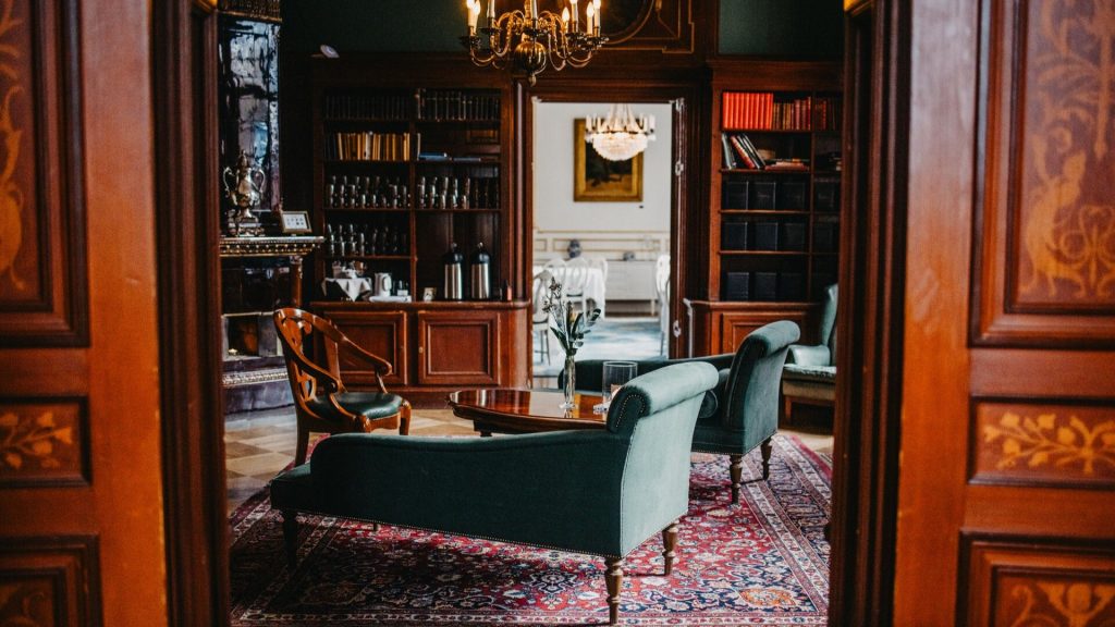 Lejondals Slotts Tea Lounge, mörka trädetaljer och bokhyllor fyllda med böcker och tekannor, koppar och tesorter. En stor kakelugn och i mitten av rummet schäslonger.